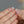 Flower-shaped earrings held between fingers against a neutral background