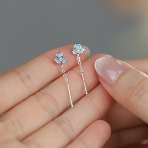 Flower-shaped earrings held between fingers against a neutral background
