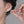Person wearing a floral earring with a hand adjusting it against a neutral background