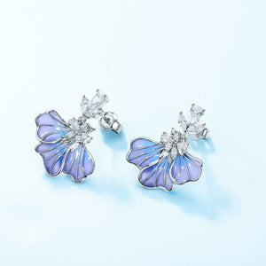 Butterfly-shaped earrings with blue wings and clear gemstones on a light blue background