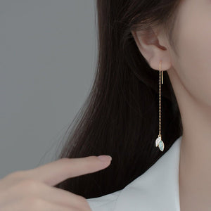 Close-up of a person wearing a gold earring with a teardrop-shaped gemstone against a neutral background.