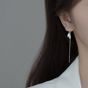Earring worn by a person with long dark hair on a plain background