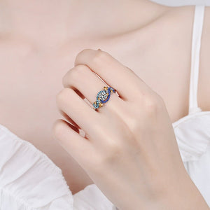 Close-up of a hand wearing a decorative ring with blue and gold elements on a light background.