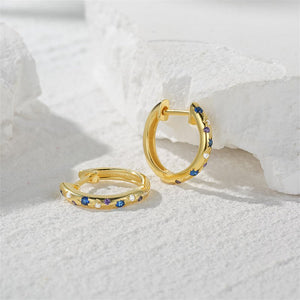 Gold hoop earrings with gemstones on a textured white surface