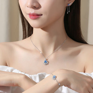 Woman wearing a necklace, earrings, and bracelet with a blue pendant.