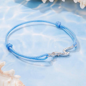 Blue braided bracelet with a silver wave-shaped charm on a light blue background