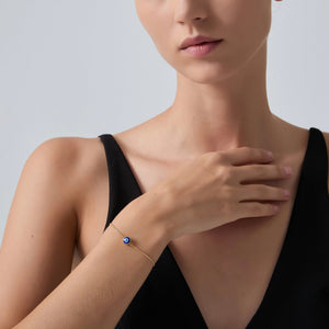 Woman wearing a gold bracelet with a blue gemstone on a plain background