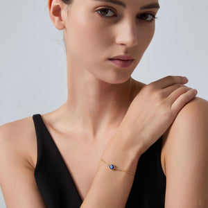 Woman wearing a delicate bracelet with a blue gemstone on a plain background