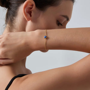 Woman wearing a gold bracelet with a blue stone on a neutral background
