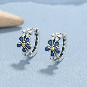 Flower-shaped earrings with blue and yellow centers on a light blue background