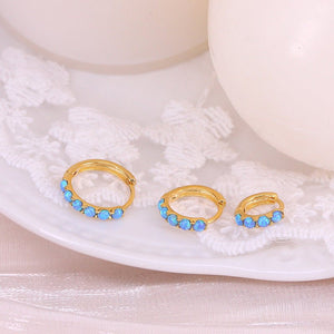 Gold hoop earrings with blue stones on a white shell