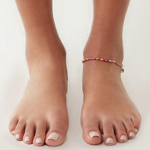 Colorful beaded anklets on feet against a white background