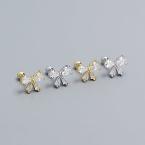 Set of bow-shaped earrings in gold and silver on a gray background