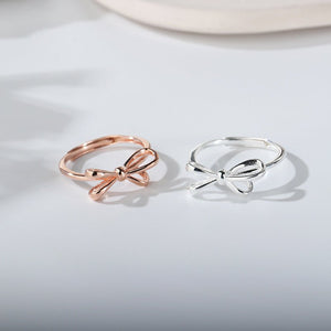 Two bow-shaped rings, one rose gold and one silver, on a light gray background.