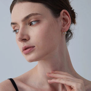 Close-up of a woman wearing a delicate earring against a neutral background