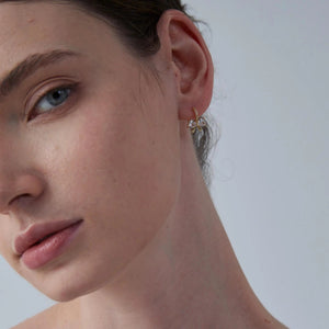 Close-up of a woman wearing a gold earring with a clear gemstone on a neutral background