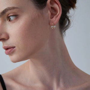 Close-up of a woman wearing a delicate earring with a clear gemstone on a neutral background
