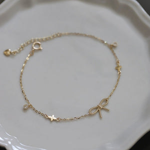 Gold bracelet with star and bow charms on a light gray plate