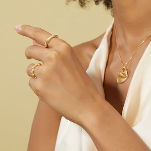 Close-up of a person wearing gold jewelry including rings and a necklace on a beige background
