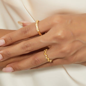Close-up of a hand wearing two gold rings on a neutral background