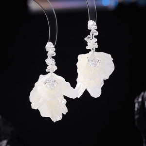 Pair of floral earrings with white petals and clear gemstones on a dark background