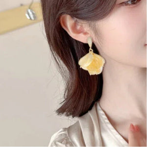 Close-up of a person wearing yellow flower-shaped earrings with a neutral background