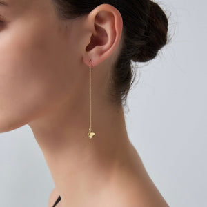 Gold chain earring with a butterfly pendant worn by a person on a neutral background