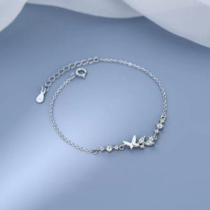 Silver bracelet with butterfly and heart charms on a light blue background