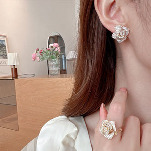 Woman wearing a pair of rose-shaped earrings and ring indoors.