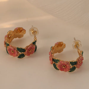Gold hoop earrings with pink floral designs on a beige background