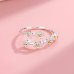 An image featuring two sterling silver rings with cherry blossom flower designs, one open band and one bypass ring, displayed on a pink background.
