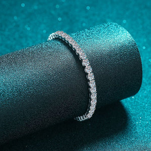 Silver bracelet on a black cylindrical stand against a teal background