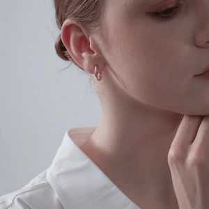 A model wearing gold-plated twisted rope hoop earrings on a white background