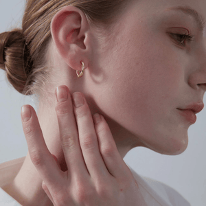 A model wearing gold-plated twisted rope hoop earrings on a white background