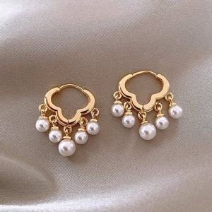 Gold hoop earrings with pearl drops on a beige fabric background