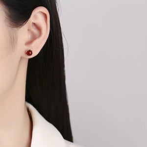 Close-up of a person wearing a red gemstone earring on a plain background