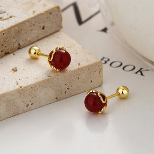 Gold earrings with red stones on a textured surface