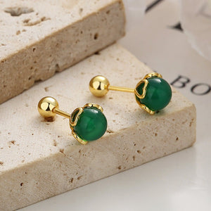 Gold earrings with green gemstones on a beige stone surface