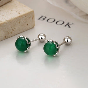 Pair of green gemstone earrings on a light surface with 'BOOK' text in the background