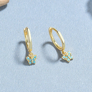 A collection of hoop earrings with butterfly charms attached, displayed against a blue background.