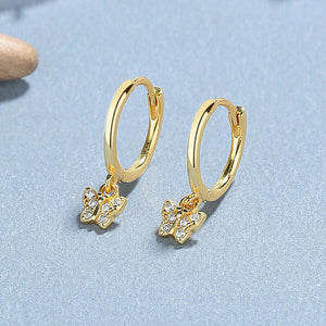 A collection of hoop earrings with butterfly charms attached, displayed against a blue background.