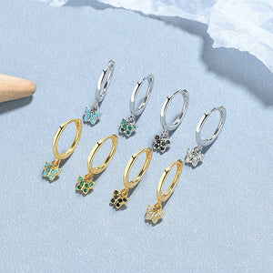 Set of gold and silver hoop earrings with various charms on a light blue background