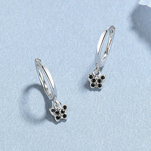 A collection of hoop earrings with butterfly charms attached, displayed against a blue background.