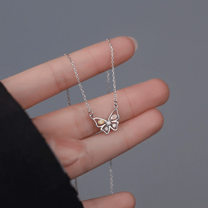 Hand holding a butterfly-shaped necklace with colorful gemstones on a gray background