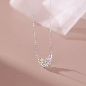 Butterfly-shaped necklace with colorful gemstones on a soft pink background
