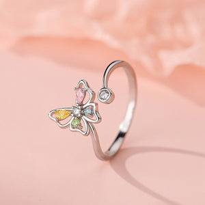 Butterfly-shaped ring with colorful gemstones on a soft pink background