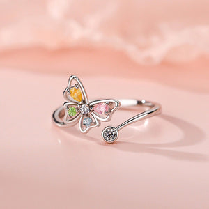 Butterfly-shaped ring with colorful gemstones on a soft pink background