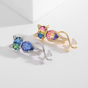 Two colorful brooches, one silver and one gold, on a light gray background.