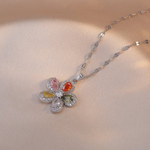 A collection of four flower pendant necklaces with gold plating, displayed on a white surface. Each pendant is crafted from titanium steel and cubic zirconia, featuring a different color combination for the gemstones.
