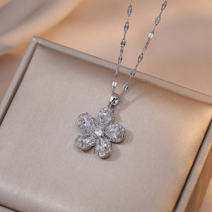 A collection of four flower pendant necklaces with gold plating, displayed on a white surface. Each pendant is crafted from titanium steel and cubic zirconia, featuring a different color combination for the gemstones.